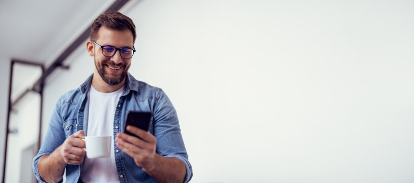 Handsome bearded man leaning on office desk, drinking coffee and talking on the phone.