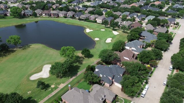 Golf course pond with golfer playing, club cars moving in upscale residential community large mansion houses concrete tiles roof, swimming pool East of Plano, Texas, Dallas Fort Worth metroplex
