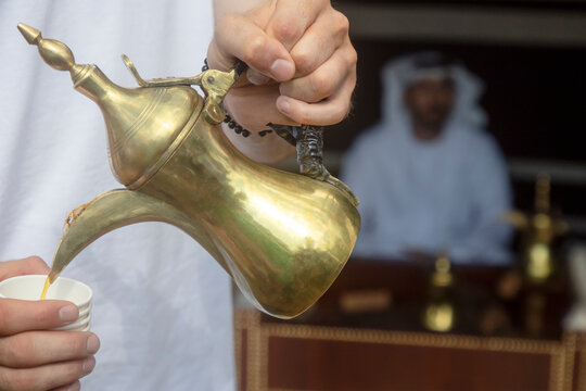 A man pours Arabic coffee into a cup from a traditional Arabic coffee pot