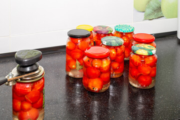 Red ripe tomatoes in glass jars and a mechanical capper. Preparing vegetables for the winter