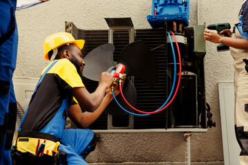 Proficient worker expertly refilling refrigerant in HVAC system while using barometer gauges to...