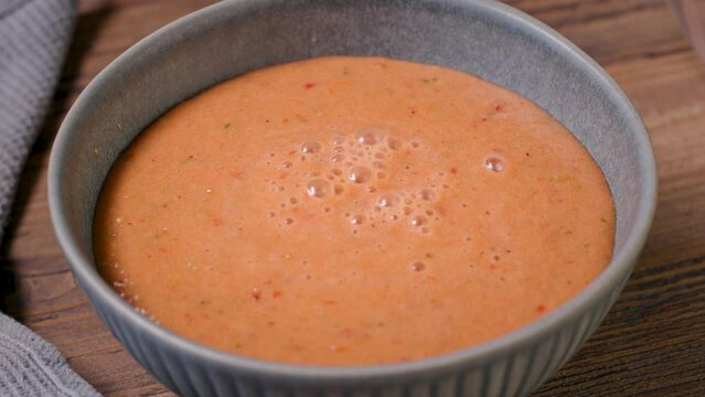 cook pours gazpacho in a bowl on wooden table, process of making fresh cold tomato soup. food closeup