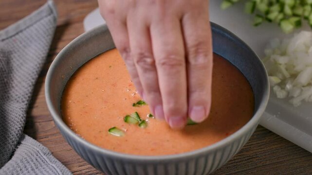 cook add chopped vegetables in a bowl of gazpacho, process of making fresh cold tomato soup. food closeup