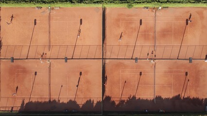 Aerial top-down view of tennis training facility camps with players and shadows