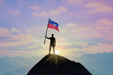 Waving flag of Haiti at the top of a mountain summit against sunset or sunrise. Haiti flag for Independence Day.
