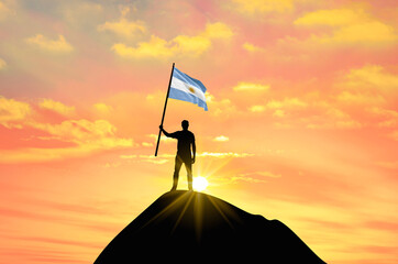 Waving flag of Argentina at the top of a mountain summit against sunset or sunrise. Argentina flag for Independence Day.