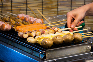 A person is cooking food on a grill with a variety of meats and vegetables