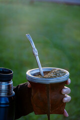 Mano de mujer sosteniendo Termo y mate, mate argentino en la naturaleza.