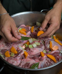  A chef meticulously prepares a hearty pork stew, adding fresh carrots, onions, and bay leaves to enhance the flavors. This image showcases the hands-on process of making a slow-cooked. 