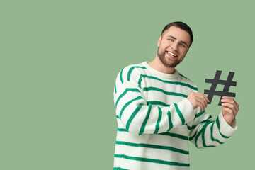 Happy young man with hashtag sign on green background