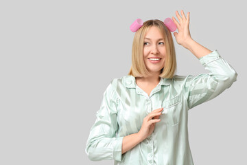Beautiful young woman with bob hairstyle and hair curlers on grey background