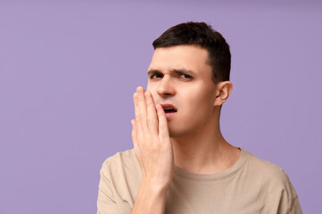 Handsome young man feeling bad smell from mouth on purple background