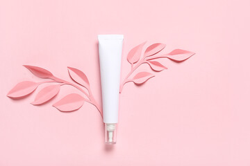 Tube of cosmetic product and paper flowers on color background