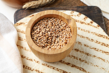 Wheat grains in wooden bowl and fresh lavash, closeup