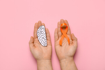 Female hands with paper brain and orange ribbon on pink background. Multiple Sclerosis Awareness...