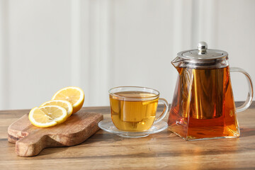 Cup of tea, teapot and board with lemon on wooden table in kitchen