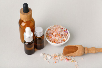 Bottles with essential oil and scattered sea salt on white background, closeup