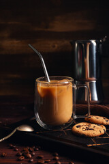 Glass of iced latte with sweet cookies and coffee beans on wooden background