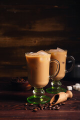 Glass cups of iced latte with cubes of sugar and coffee beans on wooden background