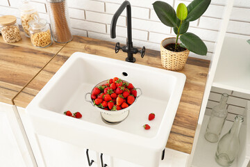 Colander with tasty strawberries in kitchen sink