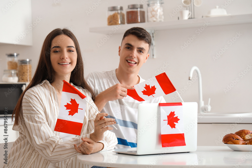 Canvas Prints young couple with flags of canada and laptop at table in kitchen