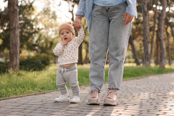 Obraz premium Mother supporting her baby while he learning to walk outdoors, closeup
