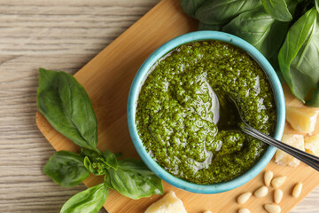 Tasty pesto sauce in bowl, basil, pine nuts and cheese on wooden table, top view