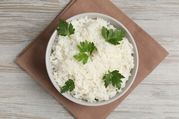 Tasty cooked rice with parsley in bowl on wooden table, top view