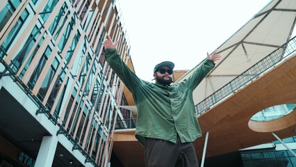 Low angle view of hipster pose in hip hop style surrounded by mall view. Portrait of sporty asian hip hop choreographer dancing break dance while looking at camera. Outdoor sport 2024. Hiphop.