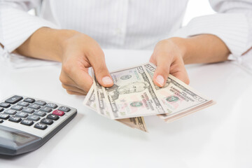 A woman is holding a stack of bills and a calculator. She is likely calculating her expenses or budget