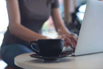 Woman working on laptop computer in coffee shop, business casual, freelance at work, people lifestyle. Black coffee cup on table, freelancer working on laptop as background