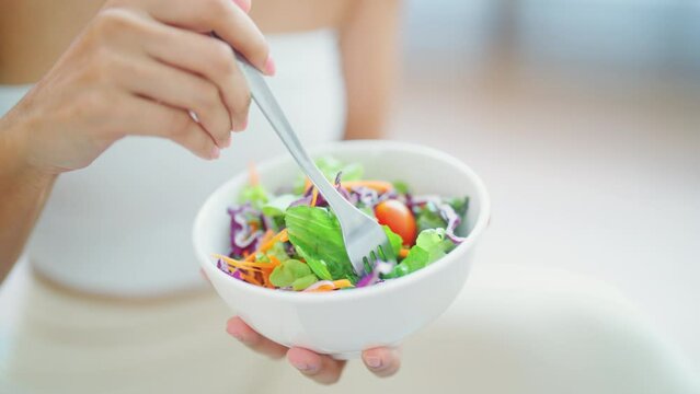 Young Asian woman holding salad bowl. Sporty girl in sportswear enjoy eat clean vegetables after exercise in house. Diet and Healthy food concept