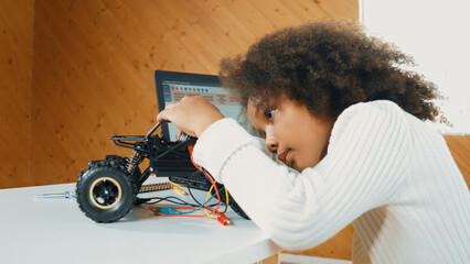 Smart african girl build robotic car while using wires while using laptop setting or writing prompt code. Skilled female student working on computer in STEM technology online classroom. Erudition.