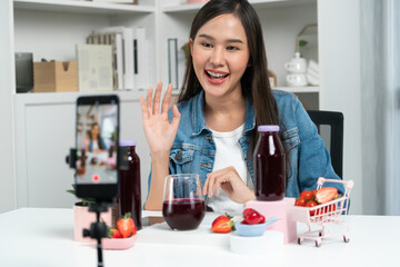 Smiling young beautiful Asian reviewing tasty mixed strawberry and cherry juice detox drinks,...