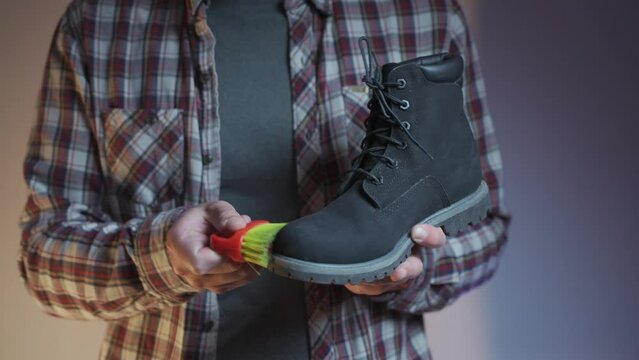 Topic care and brushing warm shoes expertly with small brush in workshop. Professional cleaning of nubuck shoes, suede autumn boots black, winter care and cleaning footwear. Boot maintenance studio. 