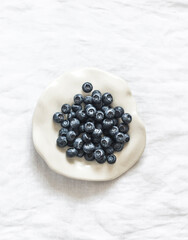 Fresh blueberries on a white ceramic plate on a light background, top view
