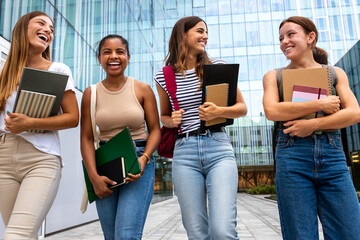 Multiracial female university student friends walking together laughing and talking. Young people...