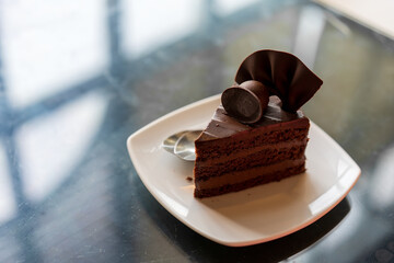iced dark chocolate cake cut of 1 piece on white plate and black marble table with spoon for sweet dessert to fatty food or snack in bakery cafe shop or restaurant with copy space