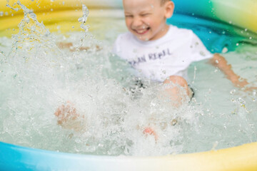 It's a hot day. A cute boy is swimming and splashing in the pool. A happy little boy smiles at the camera. Splashes of water are flying in all directions. The concept of summer holidays with children.