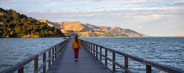long hair girl enjoys a walk on governors bay jetty at sunset; new zealand south island, canterbury...