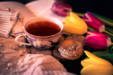 A hot cup of tea with a book, cookie, and flowers.