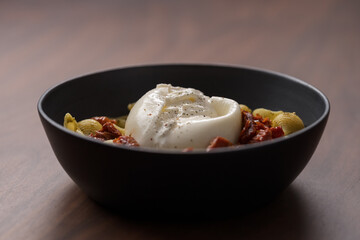 Pesto conchiglie with sundried tomatoes and burrata cheese served in black bowl