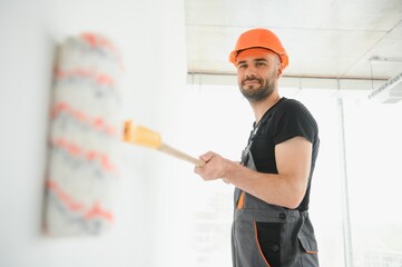 Portrait of man holding paint roller while painting white wall and making renovation