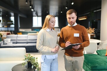 Smiling female customer looking while listening to employee discussing about sofa at store