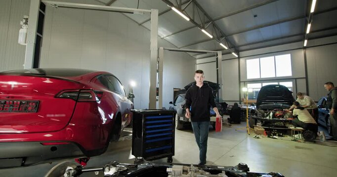 Mechanic checking electric car engines in a modern auto repair shop. Image features a red electric car and another car being repaired by technicians. EV repair concept. Auto Service, Electric engine