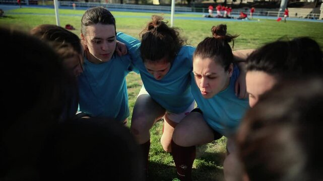 Female Rugby Team Huddling for Motivation. Determined female rugby players in blue jerseys huddling together on the field, showing unity and focus.