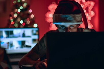 Computer hacker wearing santa hat while working on laptop late at night