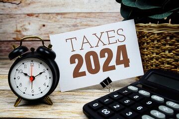Taxes 2024 text with alarm clock and calculator on wooden background