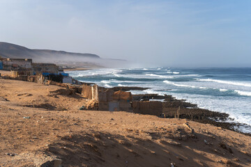 Poor Moroccan fishing village, Atlantic Ocean shore, Simple structures and sandy terrain, waves crashing on coastline