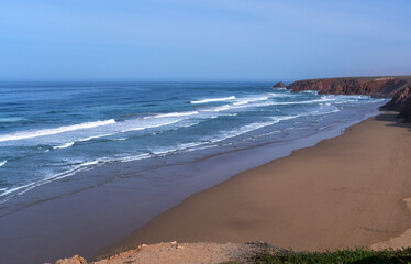 Morocco ocean coast scenic view, waves gently crashing onto a wide sandy beach, rugged cliffs frame